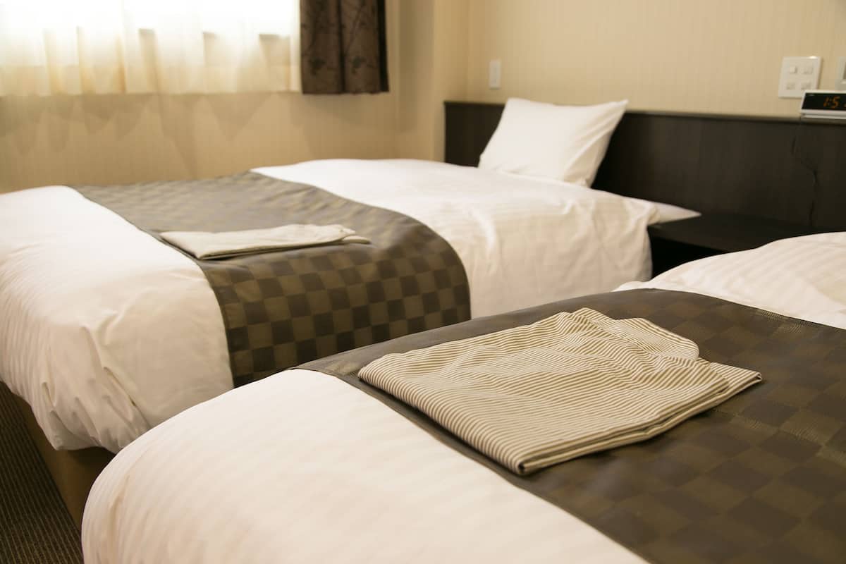 A hotel room with two single beds, a checkered bedspread, and a folded striped blanket on the bed.