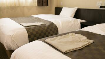 A hotel room with two single beds, a checkered bedspread, and a folded striped blanket on the bed.