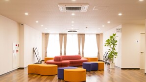 A spacious lobby with a red sofa, orange and purple ottomans, and a potted plant. - Okawa Riverside Hotel (Okawa)