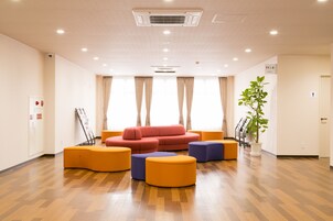 Un vestíbulo amplio con un sofá rojo, otomanas naranja y moradas, y una planta en maceta.