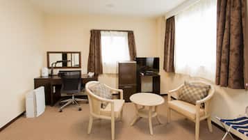 Una habitación de hotel con escritorio, dos sillones, una pequeña mesa redonda, televisor y minibar.