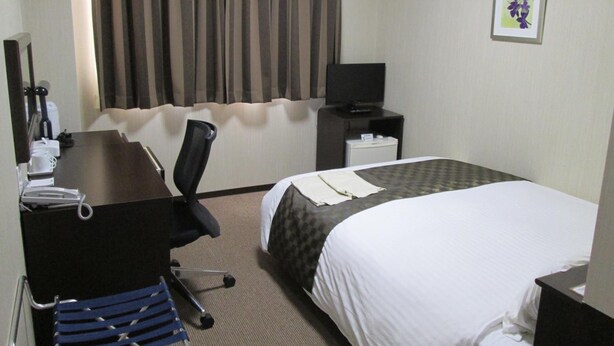 Habitación de hotel con cama, escritorio con silla, televisor y una mesita con lámpara.