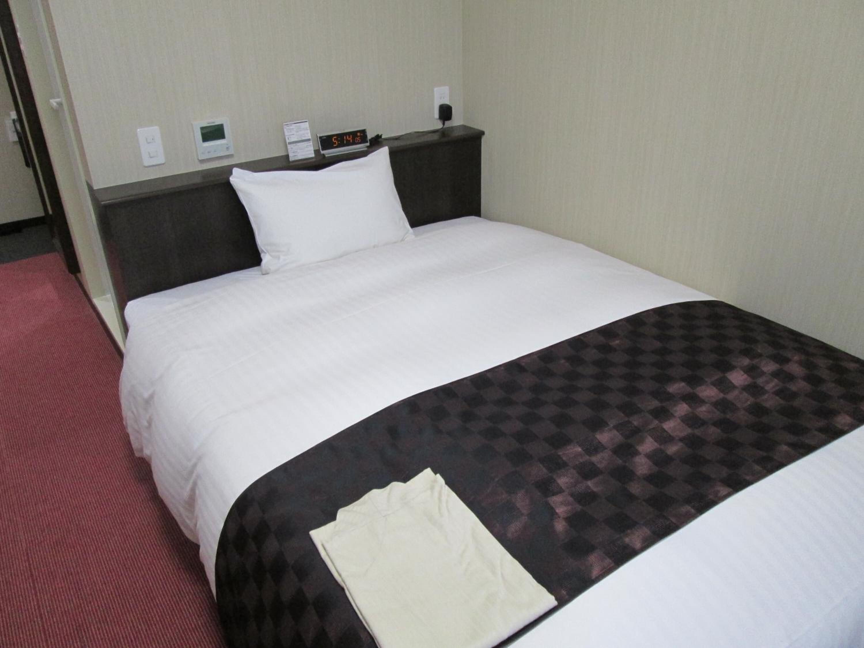 Una habitación de hotel con cama, mesita de noche, reloj digital y alfombra roja.