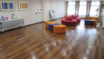 A spacious room with a wooden floor, a desk with a computer, colorful seating, and a window with curtains.