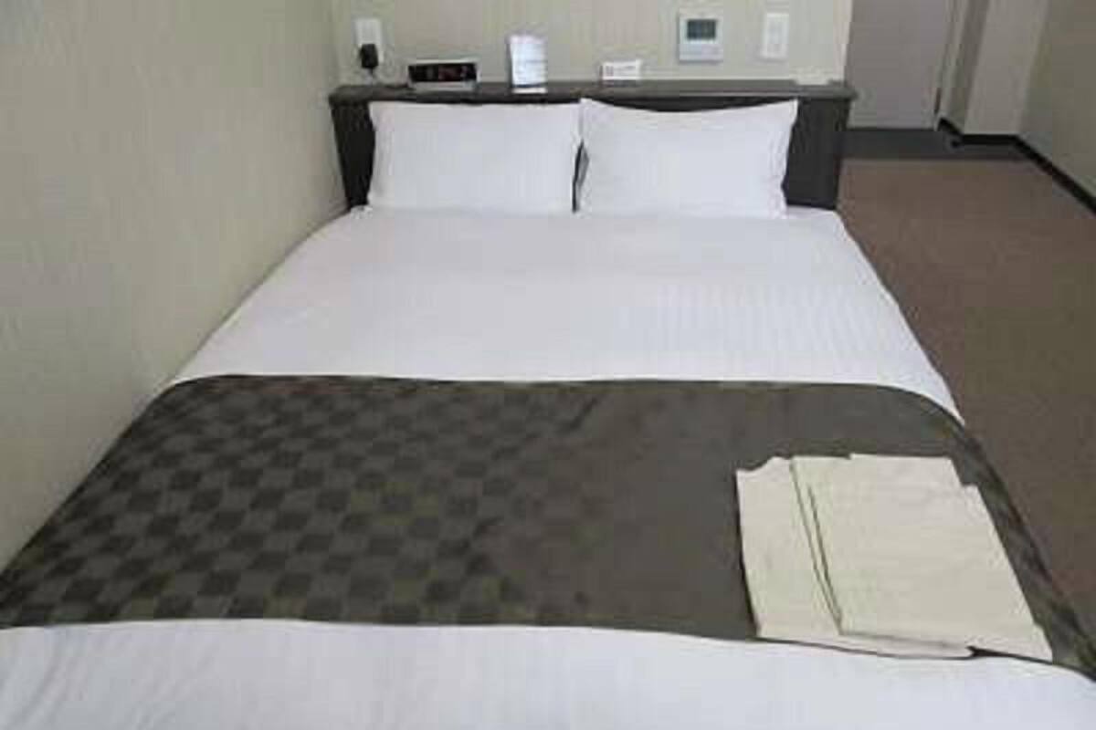 A hotel room with a bed, a nightstand, and a wall-mounted thermostat.