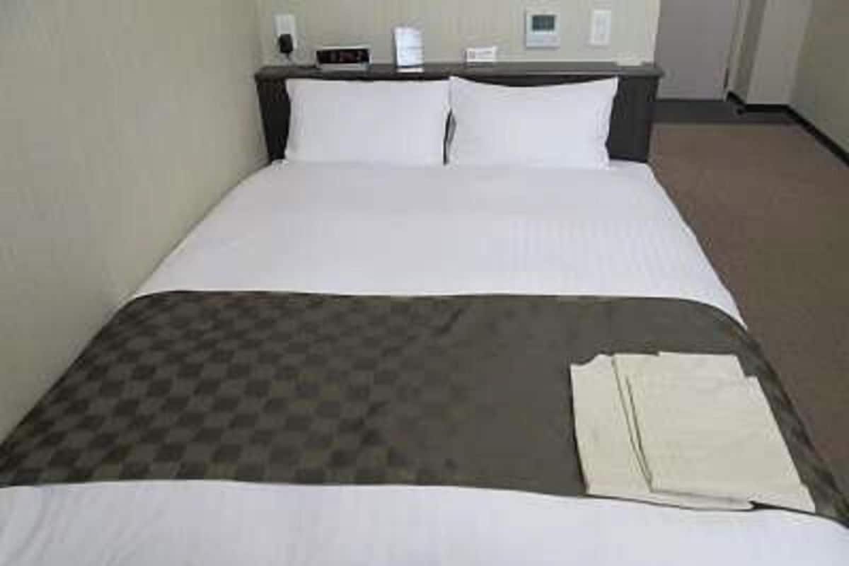 Quarto de hotel com cama, mesa de cabeceira e termostato fixado na parede.