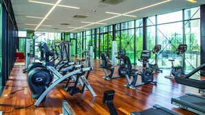 Un gimnasio moderno con máquinas de cardio, estaciones de pesas y amplias ventanas que ofrecen luz natural y vistas al verdor.
