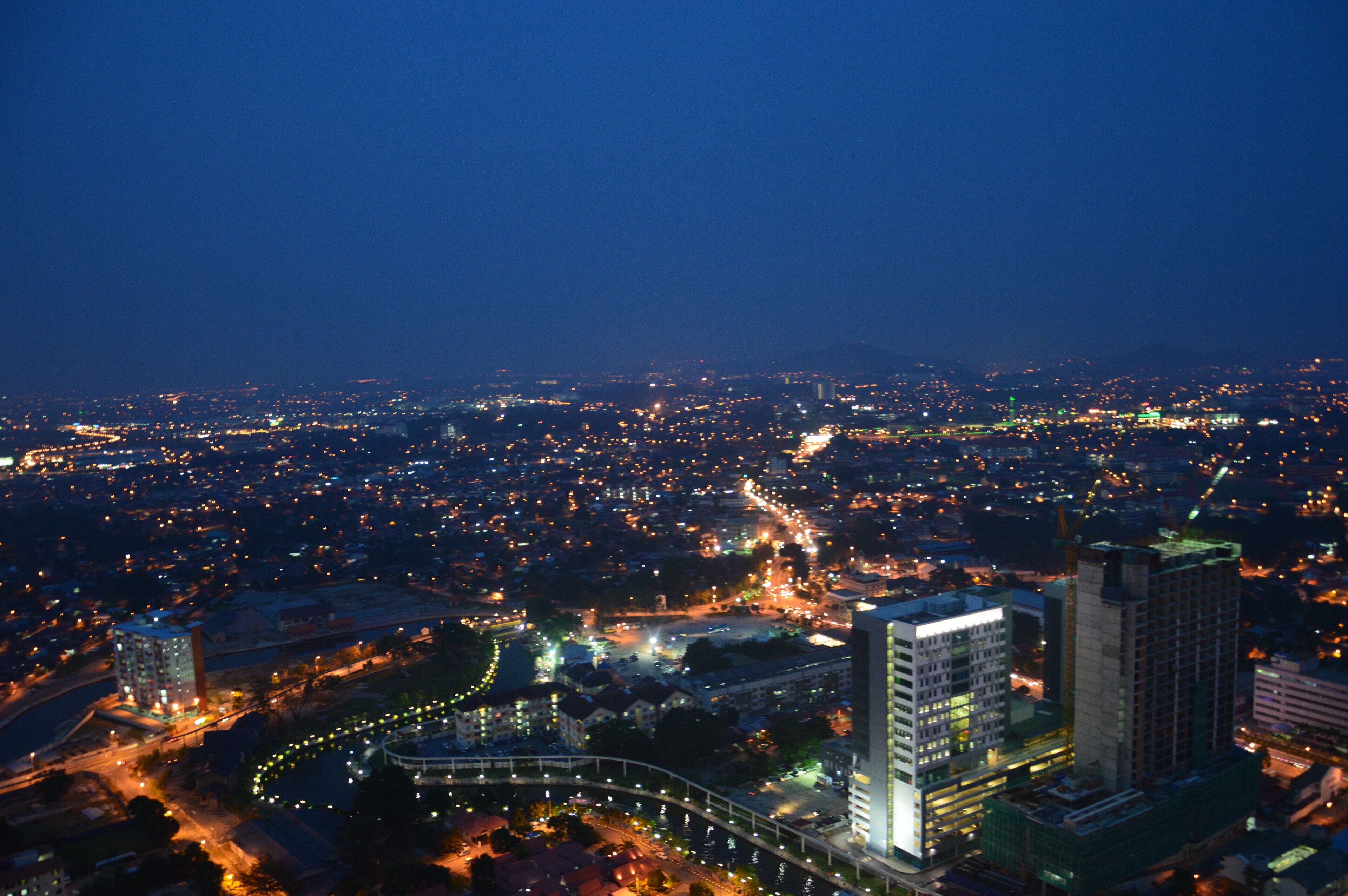 A nighttime cityscape with illuminated buildings and a winding road.