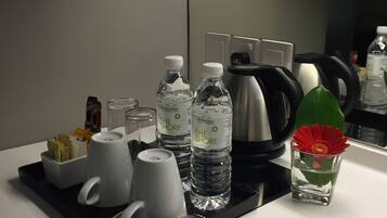 Mostrador de hotel con una bandeja que contiene una cafetera, dos botellas de agua, una taza, una taza de café y un pequeño jarrón con una flor.