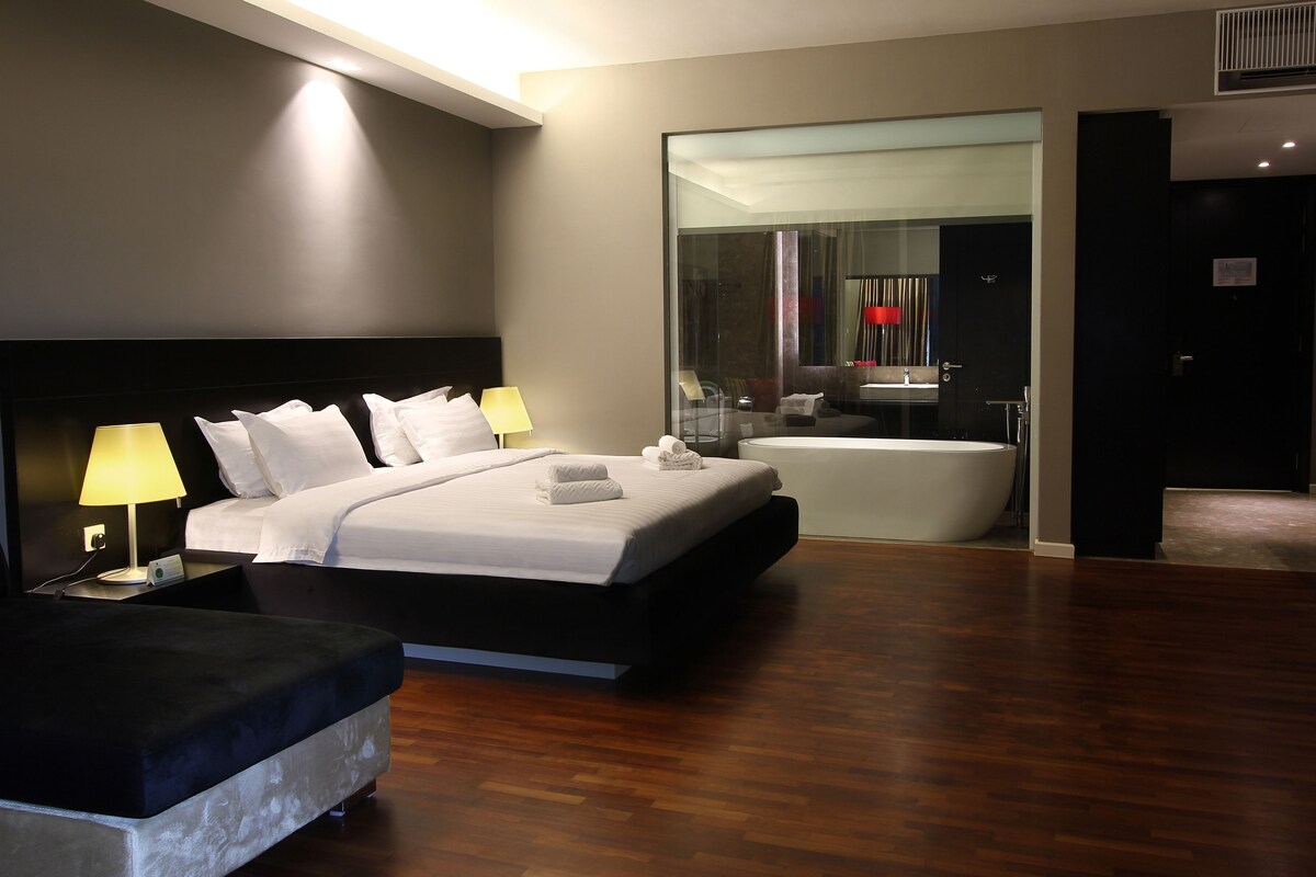 A modern hotel room with a large bed, bedside lamps, a bathtub, and a large mirror.
