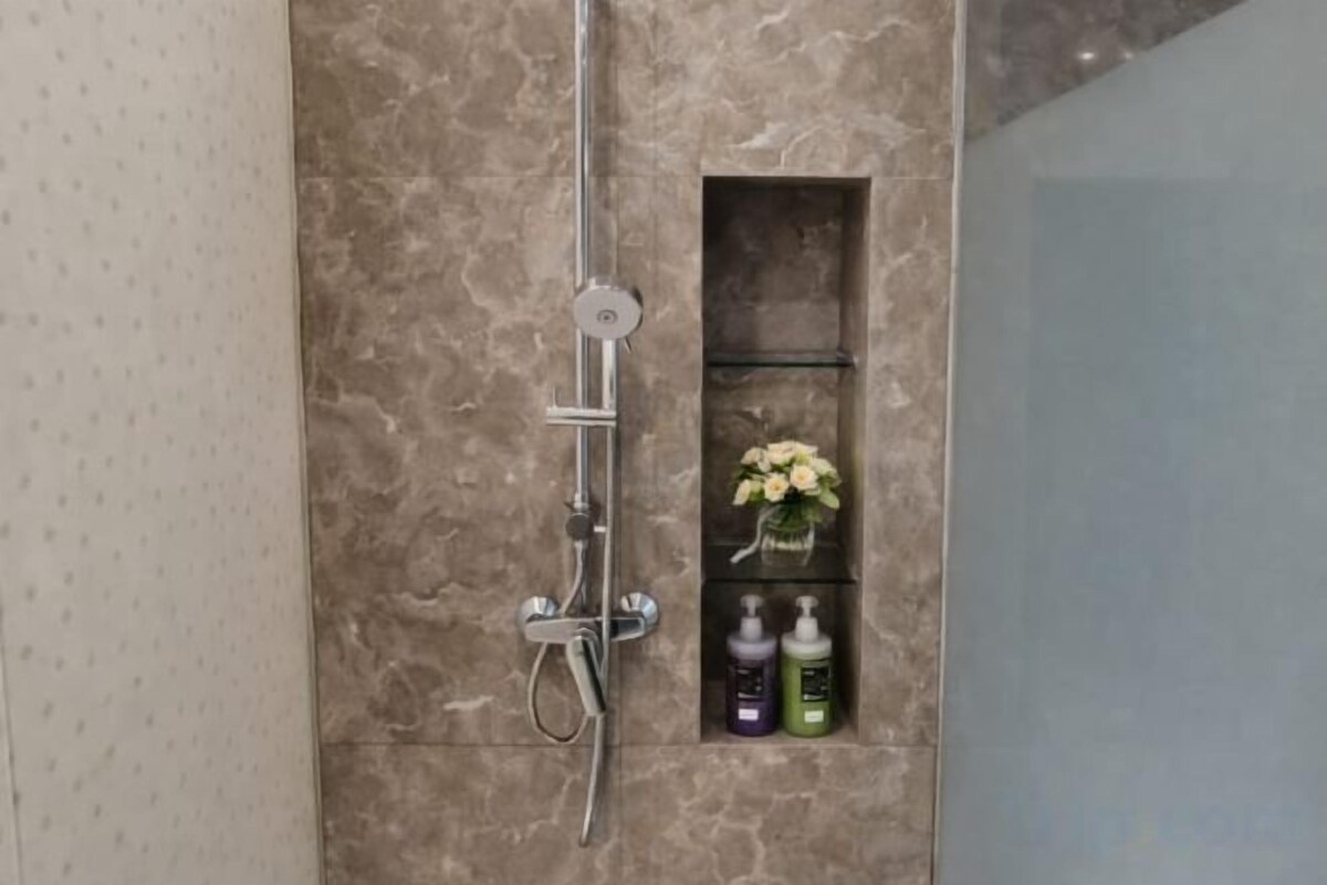 Un baño con ducha, estante para artículos de aseo y pared de mármol.