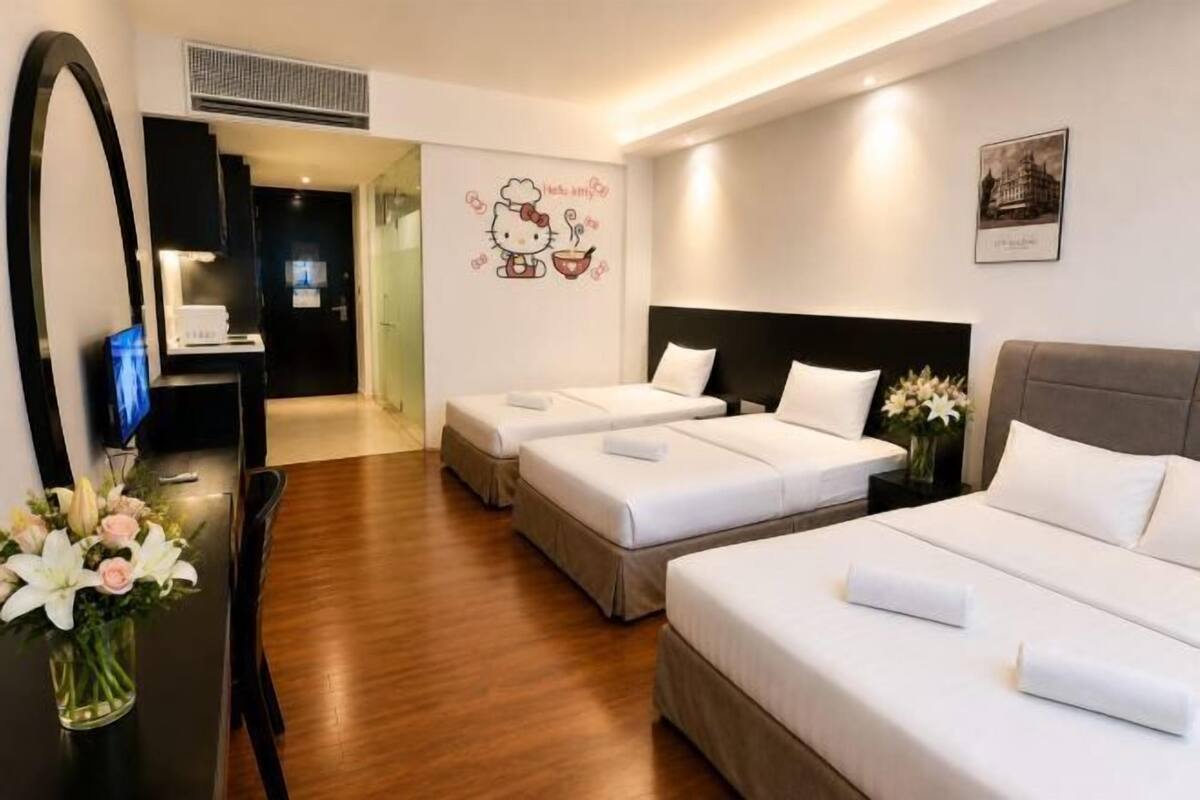 Habitación de hotel con dos camas individuales, un escritorio con ordenador, un espejo y una decoración de Hello Kitty en la pared.