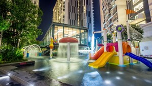 Zona de juegos acuáticos con toboganes y chorros de agua, rodeada de edificios altos y vegetación.