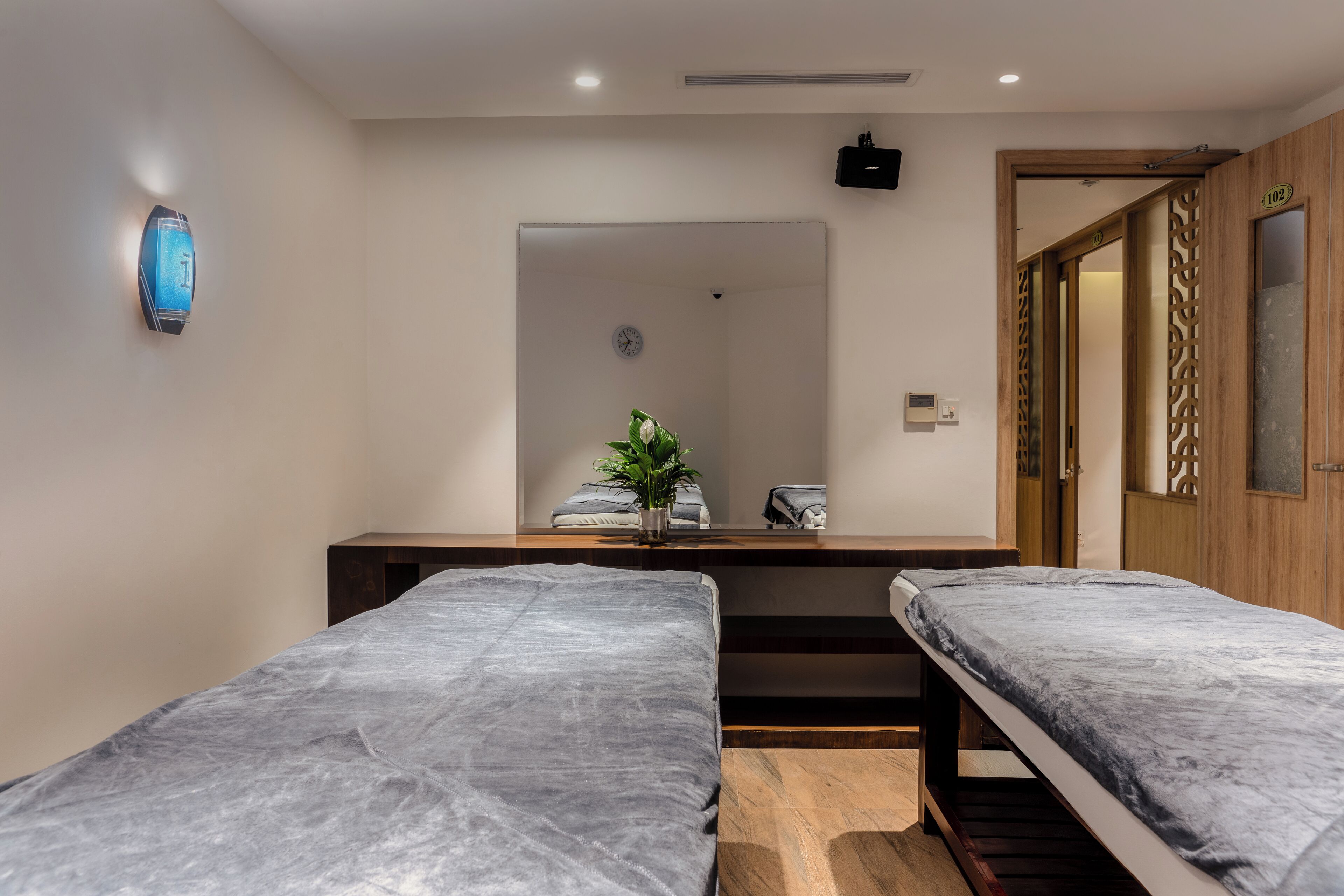 A room with two beds, a small table with a plant, and a mirror.
