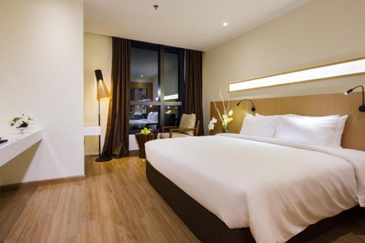Ein Hotelzimmer mit einem großen Bett, einem Schreibtisch, einem Stuhl und einem Vorhangfenster.