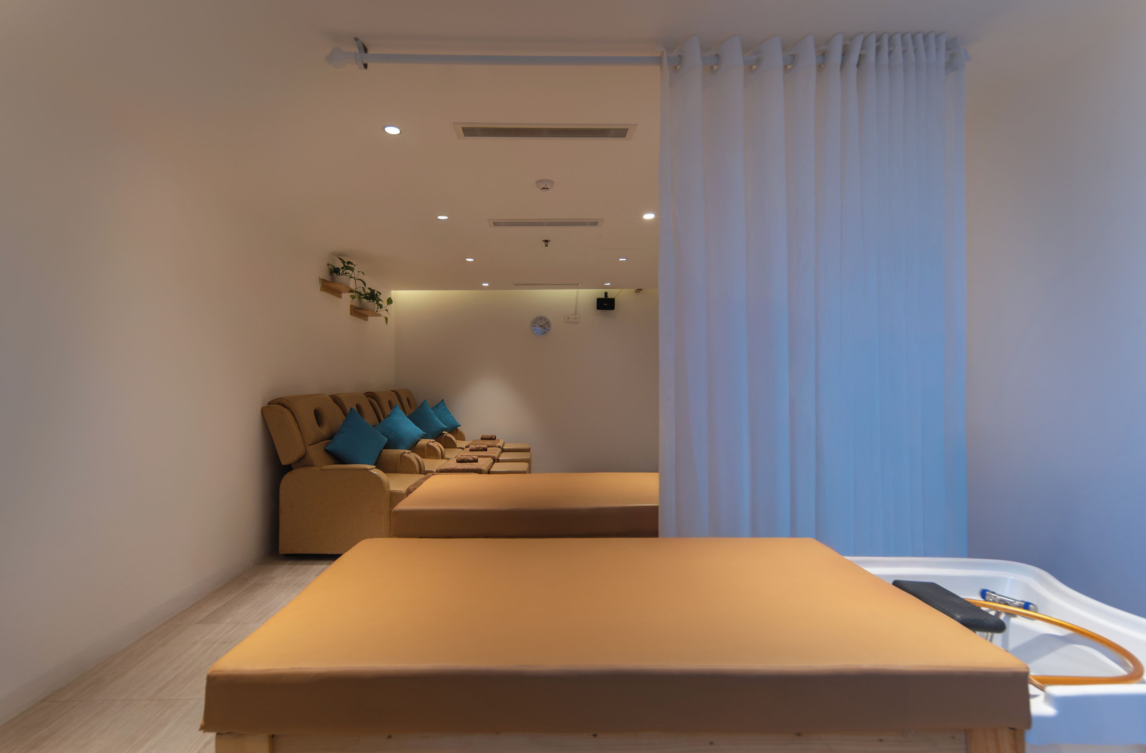 A modern room with a bed, a sofa, and a small table. There are ceiling lights and a clock on the wall.