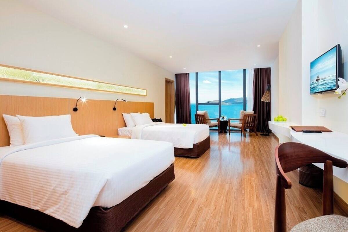 Une chambre d’hôtel avec deux lits, un bureau, une chaise, une télévision et une grande fenêtre donnant sur un beau paysage.