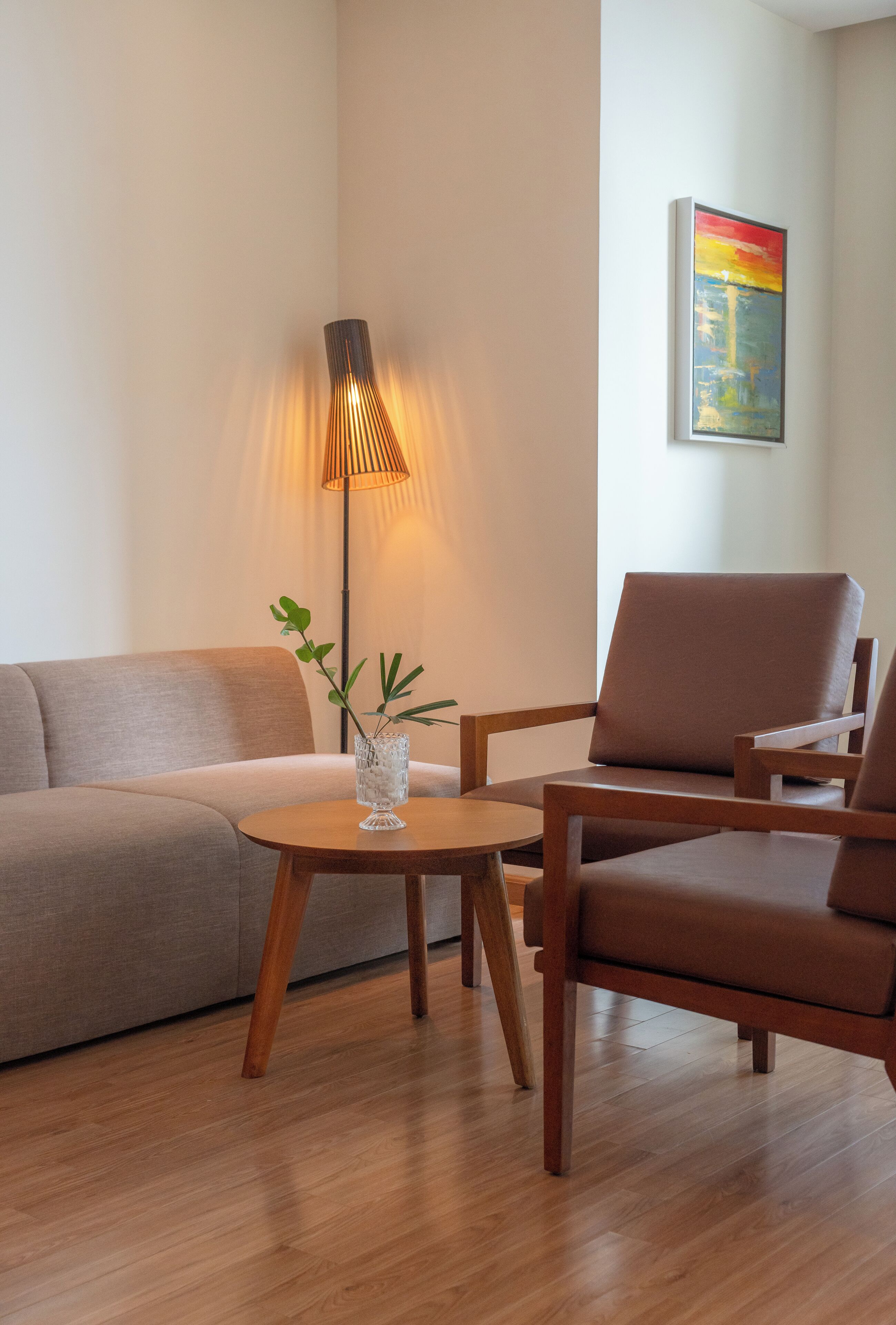 Una sala de estar moderna con un sofá, dos sillones, una mesita, una lámpara de pie y un cuadro en la pared.