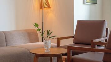 Een moderne woonkamer met een bank, twee stoelen, een klein tafeltje, een vloerlamp en een schilderij aan de muur.