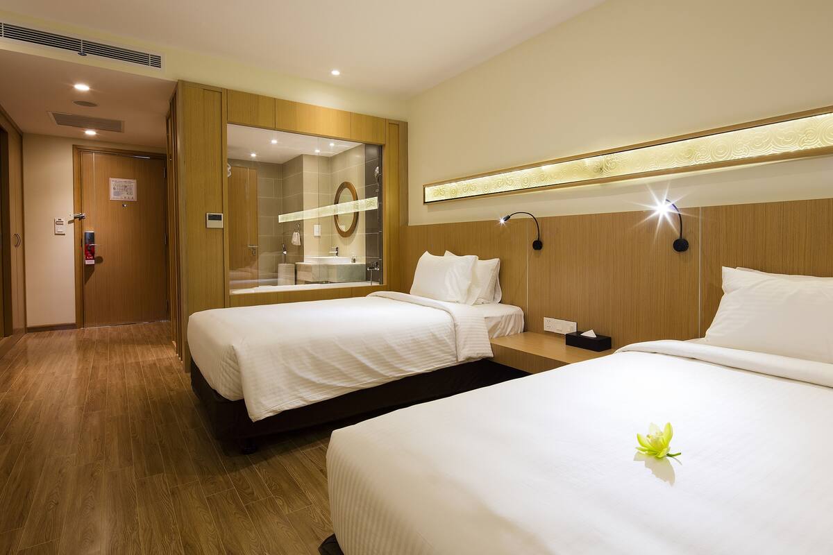 Une chambre d’hôtel avec deux lits, un grand miroir, une table de chevet et une tête de lit en bois.