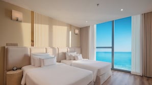 Hotelkamer met twee bedden, een rond bijzettafeltje, een groot raam met uitzicht op zee en een modern design.