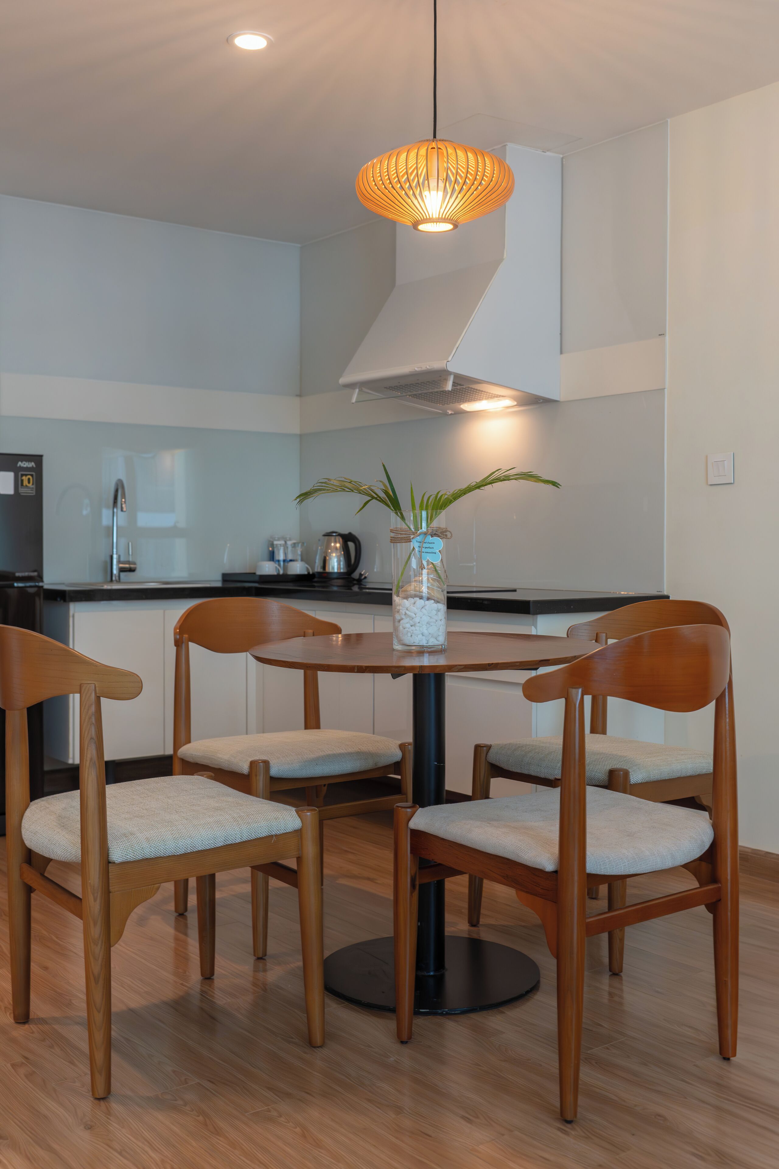 Een moderne keuken met een ronde tafel, vier houten stoelen, een hanglamp en een plant in een glazen pot.