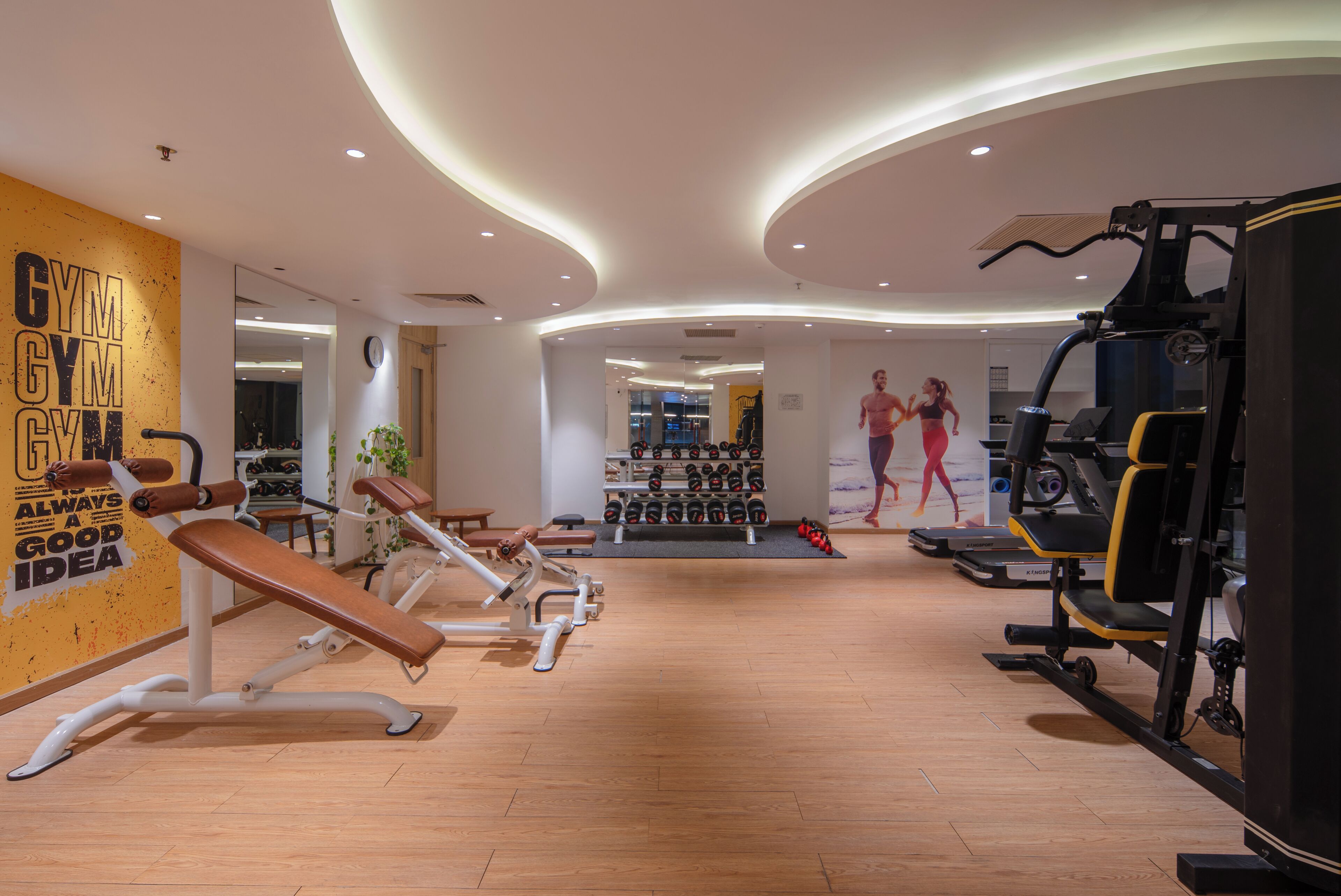 Una palestra moderna con attrezzatura cardio, rastrelliere per pesi e una parete motivazionale.