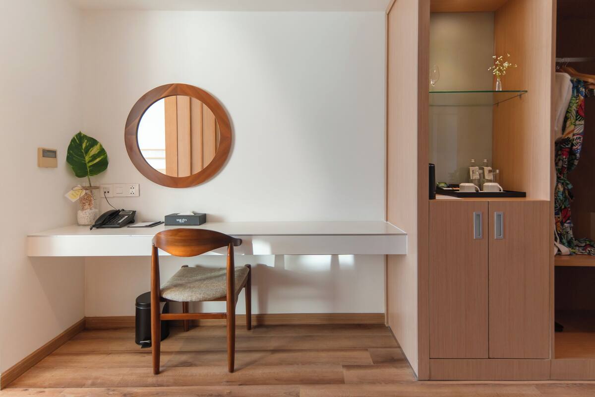Une chambre moderne avec un bureau en bois, une chaise, un miroir rond, une petite plante et une armoire.
