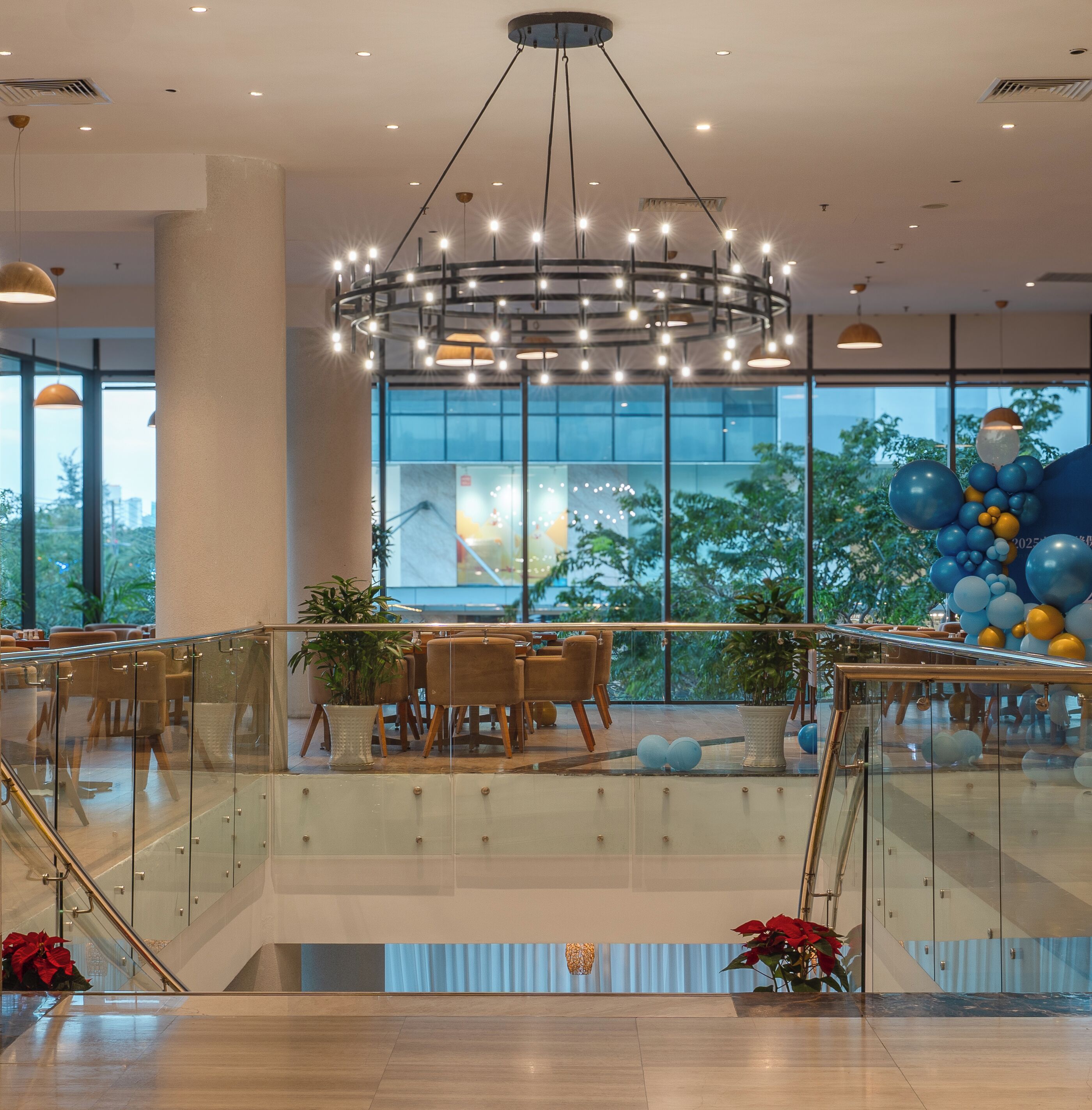 Amplio espacio interior con una lámpara moderna, barandillas de cristal y vistas a zonas verdes.