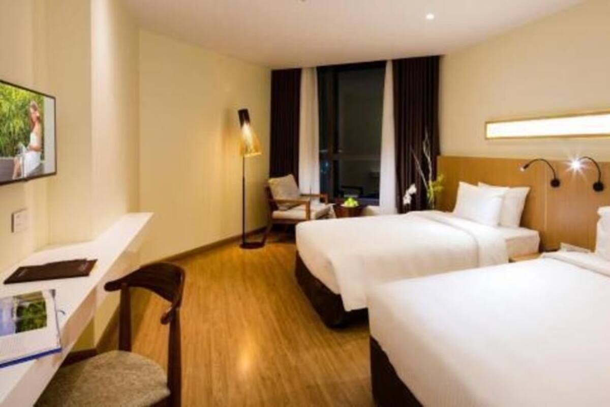 Ein Hotelzimmer mit zwei Betten, einem Schreibtisch, einem Stuhl, einer Lampe und einem Fenster.