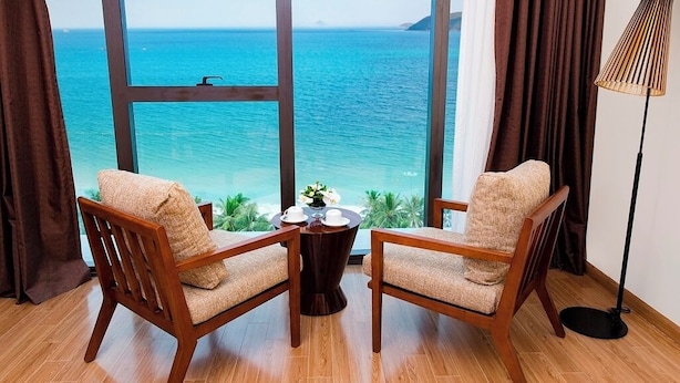 Een kamer met twee houten stoelen gericht op een groot raam met uitzicht op een strand.
