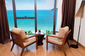 A room with two wooden chairs facing a large window overlooking a beach. - Starcity Bayfront Nha Trang Hotel (Nha Trang)