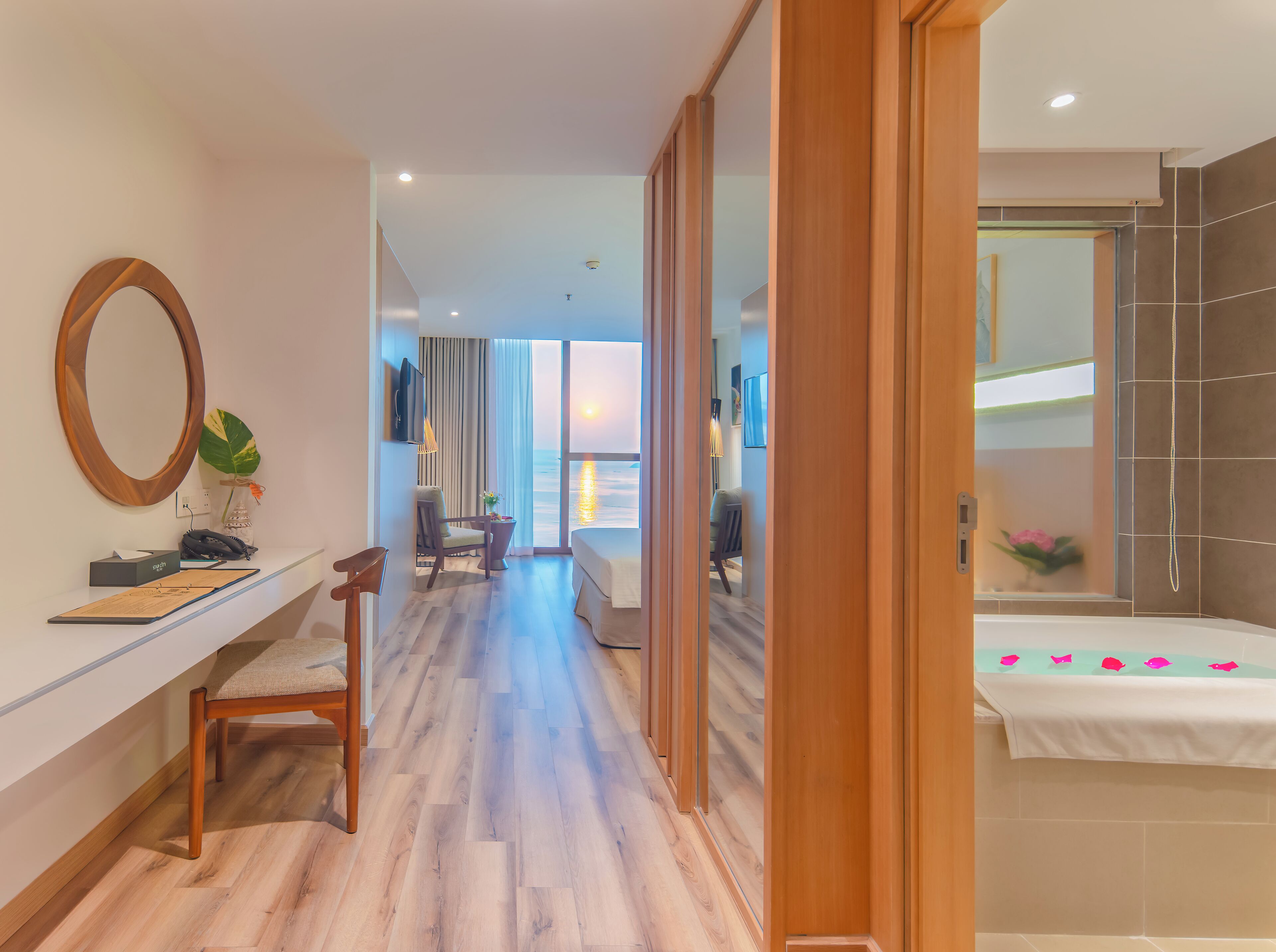 A hotel room with a wooden desk, a chair, a bed, and a view of the ocean.