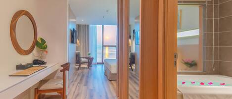 A hotel room with a wooden desk, a chair, a bed, and a view of the ocean.