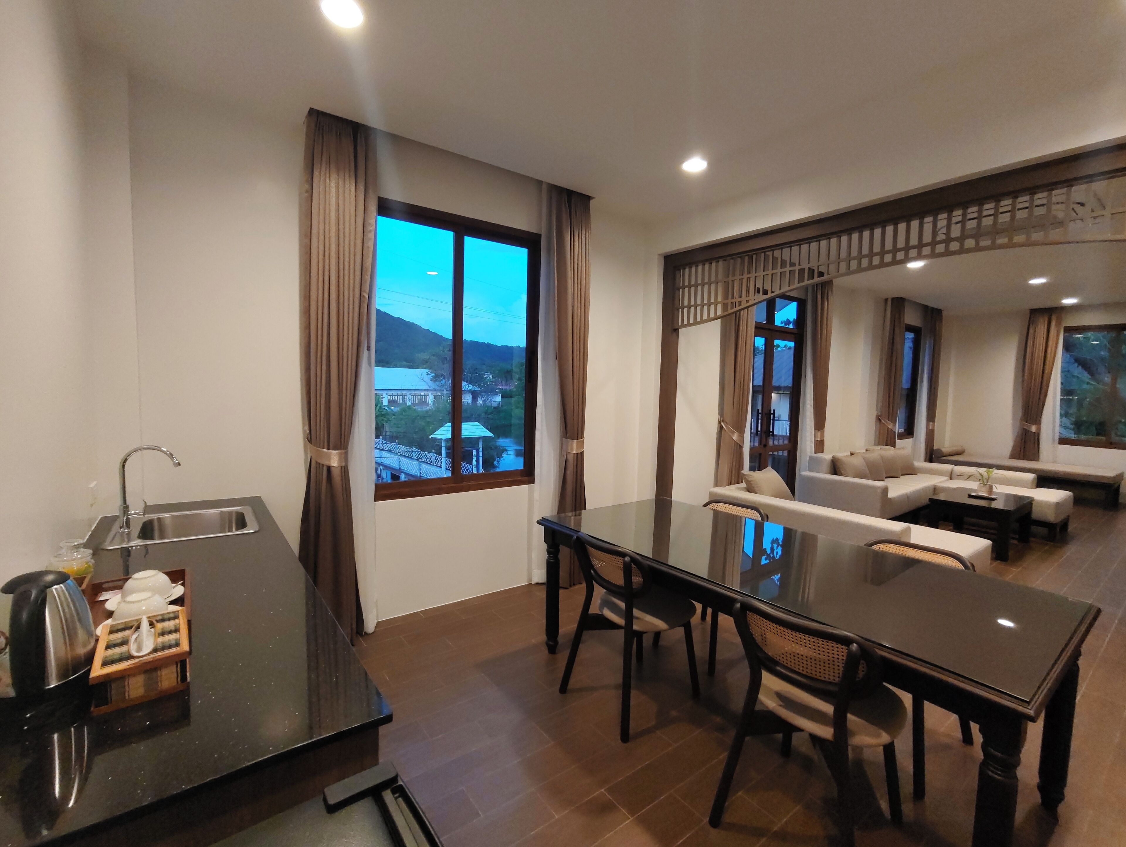 Een moderne hotelkamer met een zithoek, een keuken met een spoelbak en een groot raam met uitzicht op een bergachtig landschap.