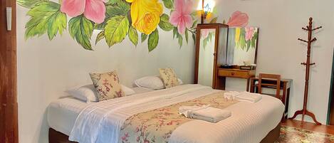 Una habitación de hotel con una cama grande, decoración floral en la pared, una mesita de noche de madera, un espejo y una lámpara de pie.