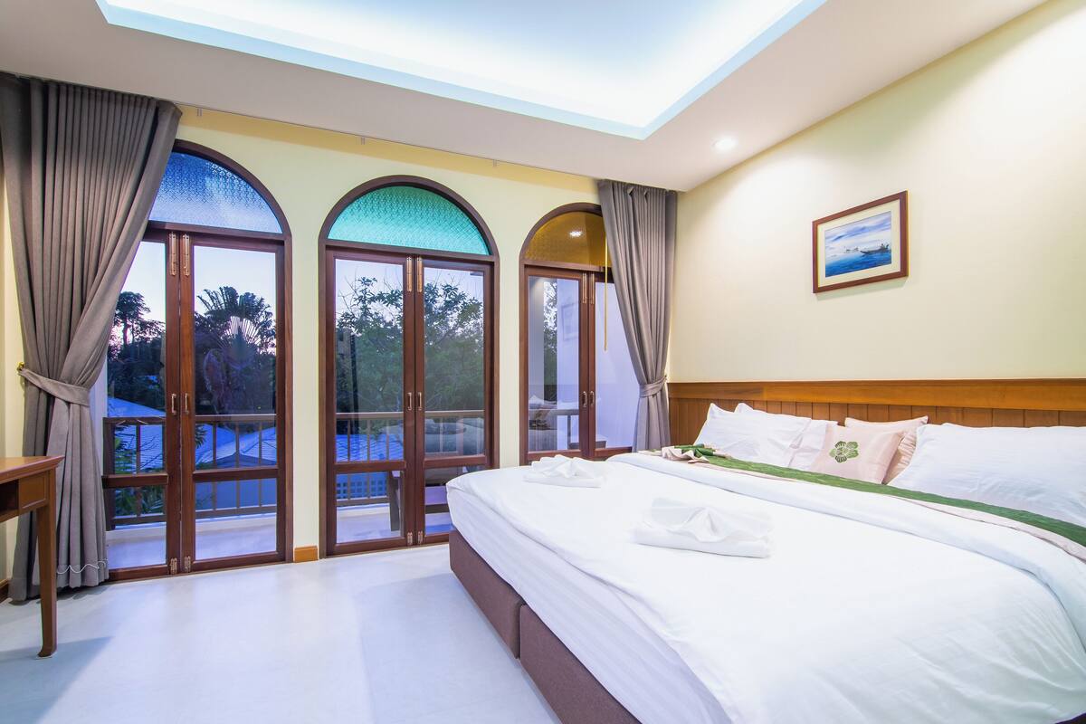 Une chambre d’hôtel avec un grand lit, une tête de lit en bois et une vue sur l’extérieur grâce à des portes vitrées en arc de cercle.