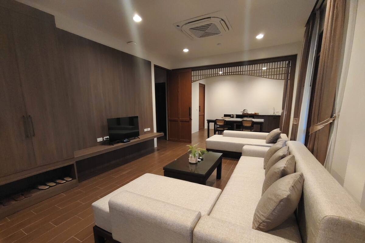 Un salon moderne avec un canapé, une table basse et un téléviseur posé sur un meuble. On aperçoit à l’arrière-plan un coin repas avec une table et des chaises.