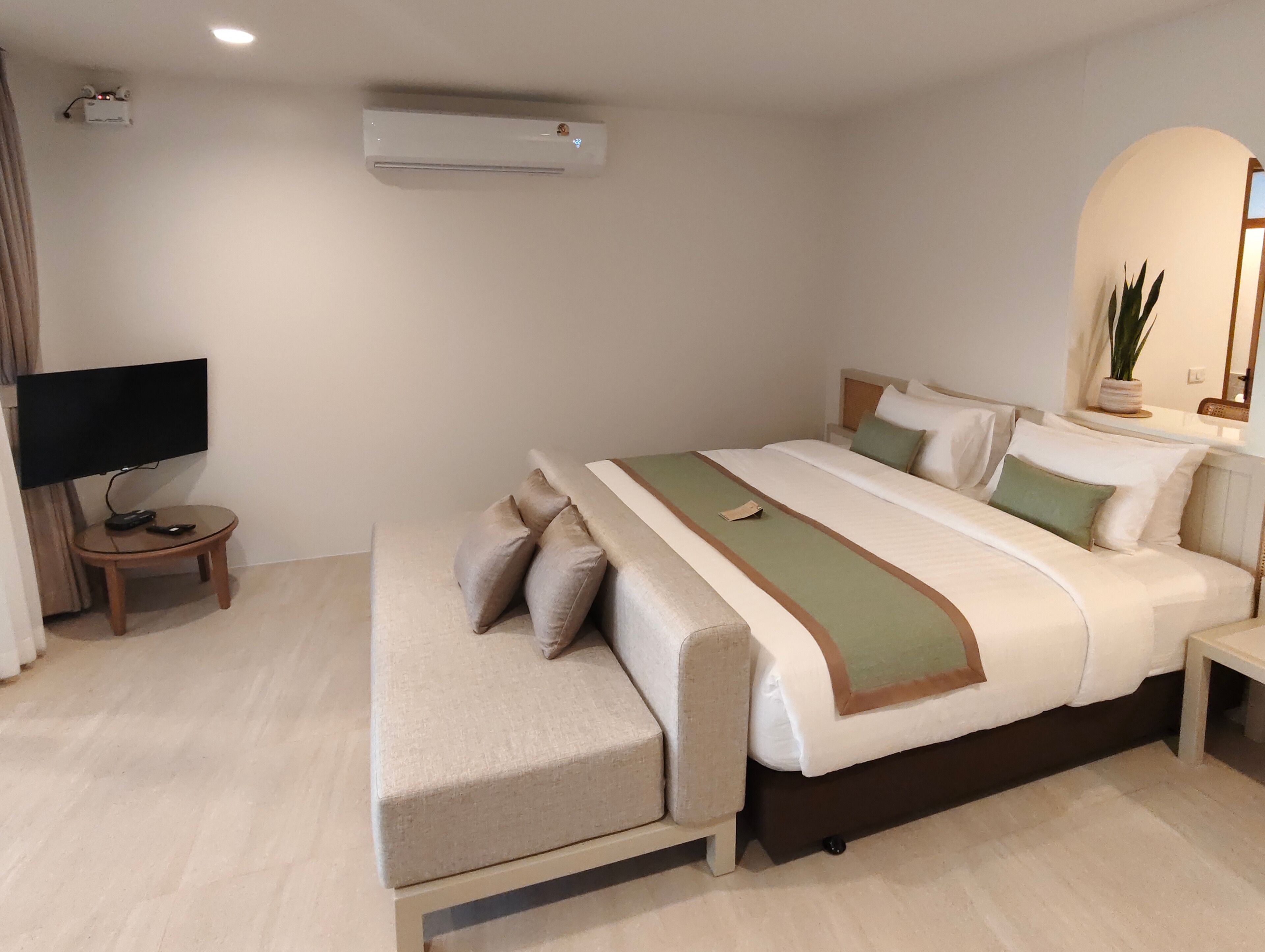 A hotel room with a bed, bedside tables, a TV, and an air conditioning unit.