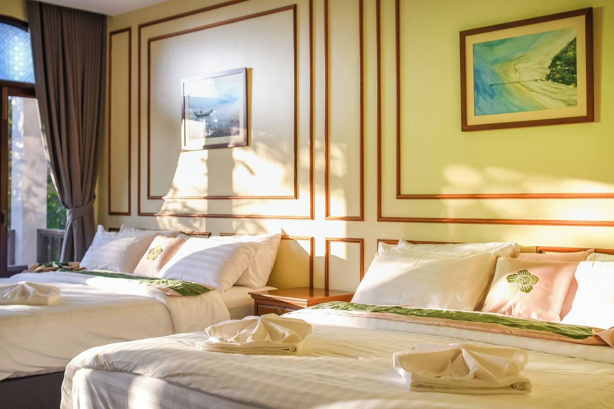 Une chambre d’hôtel avec deux lits, un tableau au mur et une fenêtre avec des rideaux.