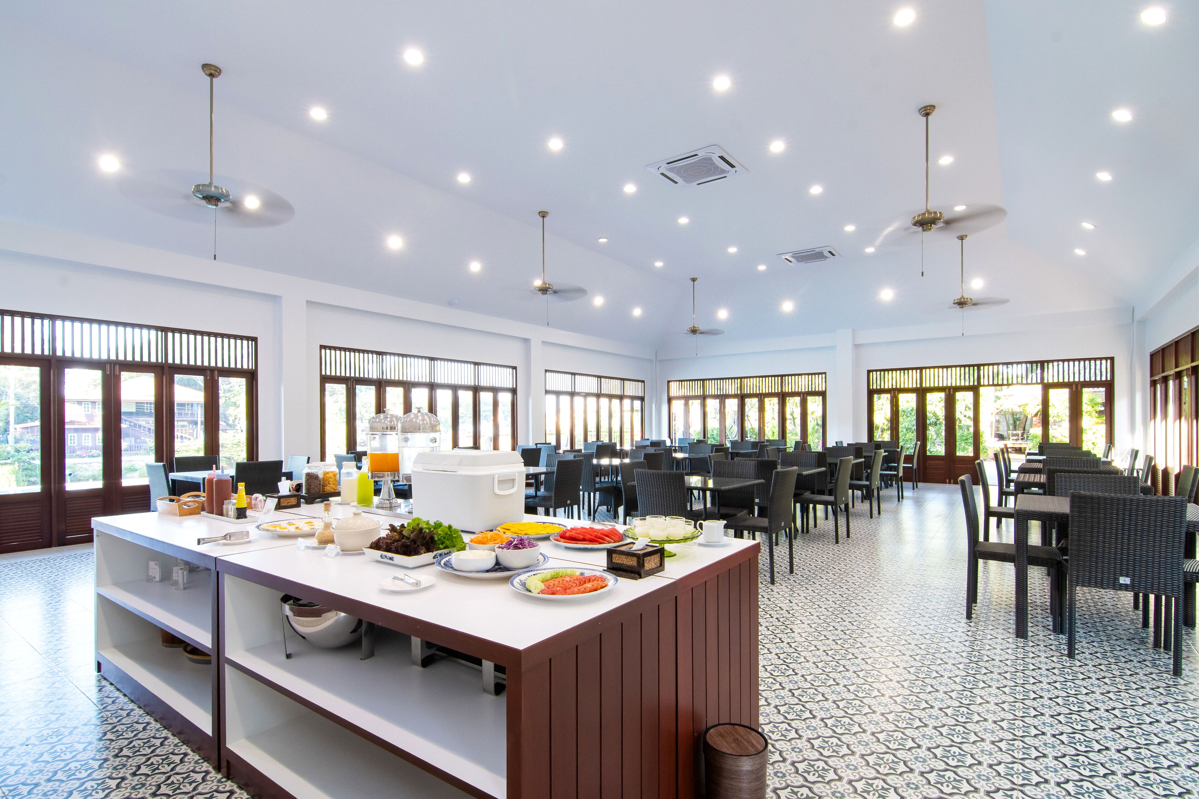 Un comedor amplio con una mesa buffet central, varias luces de techo y ventanas grandes que dejan entrar luz natural.