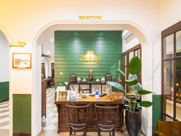 Een receptiegedeelte met een groene wand, een receptiebalie, twee stoelen en een grote potplant.