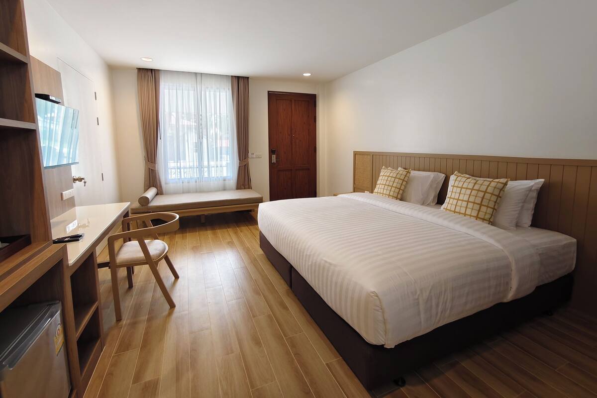 Une chambre d’hôtel avec un lit, un bureau, une chaise, une fenêtre avec des rideaux et une porte.