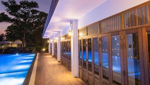 Un área junto a la piscina con terraza de madera, ventanas grandes y vistas al agua.