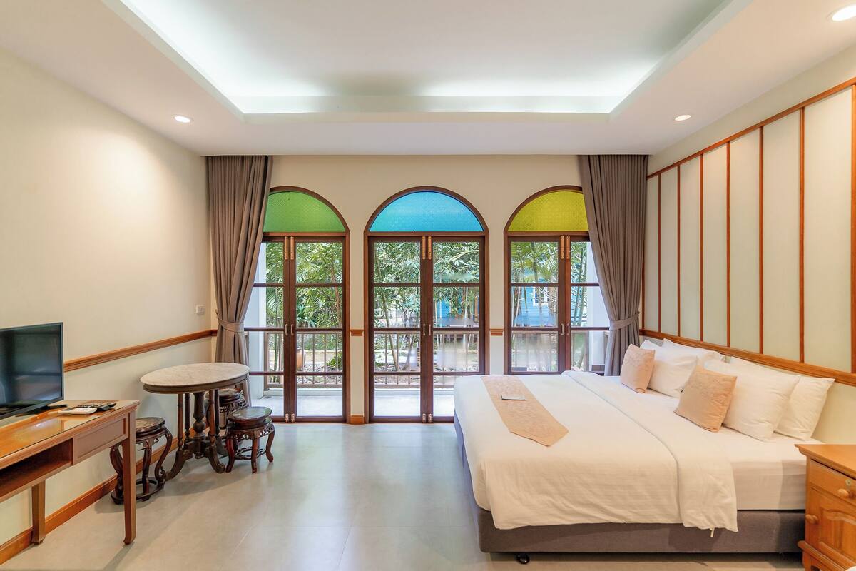 Une chambre d’hôtel avec un grand lit, une télévision, une petite table et une vue sur l’extérieur grâce à des fenêtres en arc de cercle.