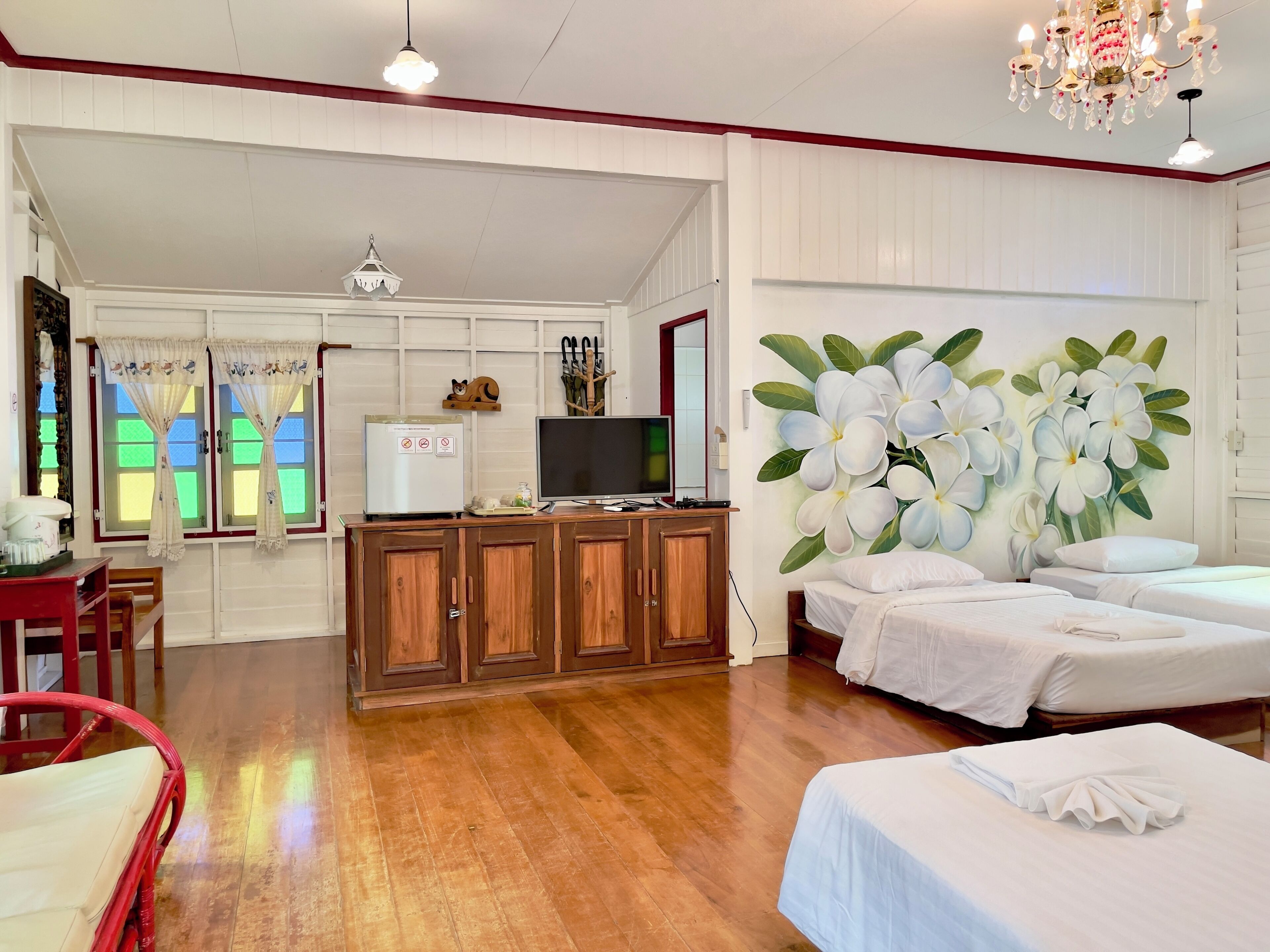 Quarto de hotel com piso de madeira, TV sobre um móvel de madeira, cama com roupa de cama branca e um mural floral de flores brancas na parede.