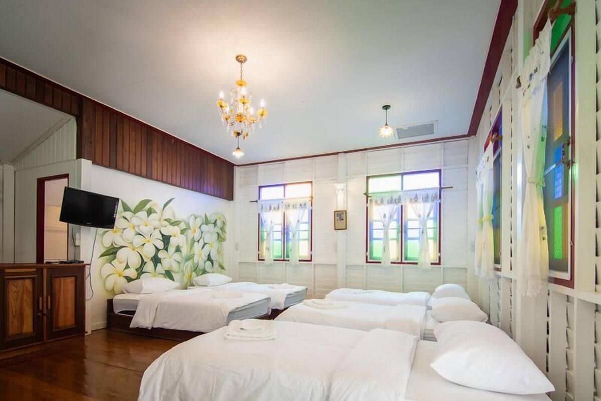 Une chambre d’hôtel avec plusieurs lits, un lustre, une télévision et un mur orné d’une fresque florale.