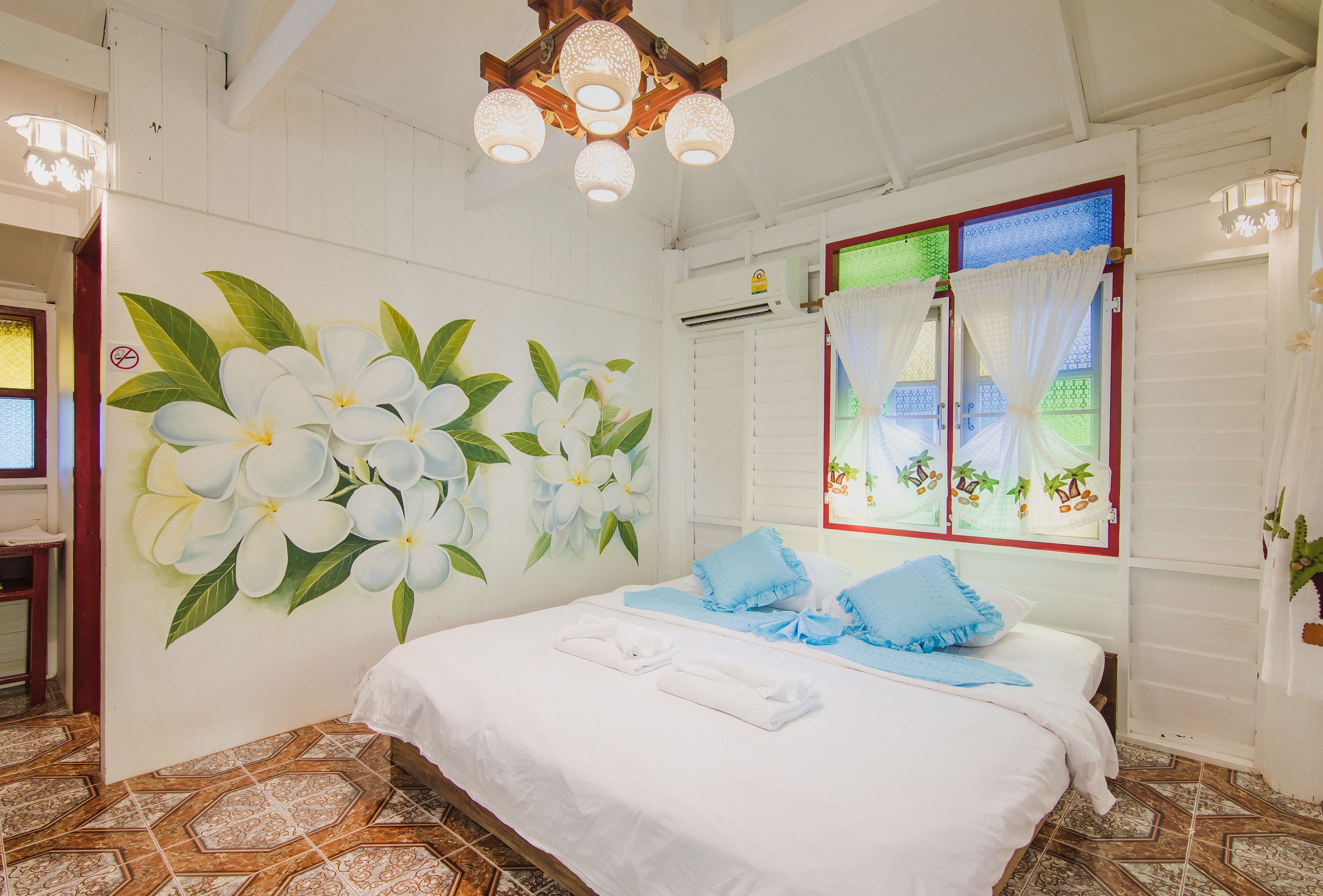 A bedroom with a bed, white walls, a floral mural, a window with curtains, and a tiled floor.