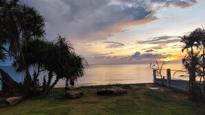 Vista de un atardecer sobre un mar tranquilo, con palmeras y una zona cubierta de hierba.