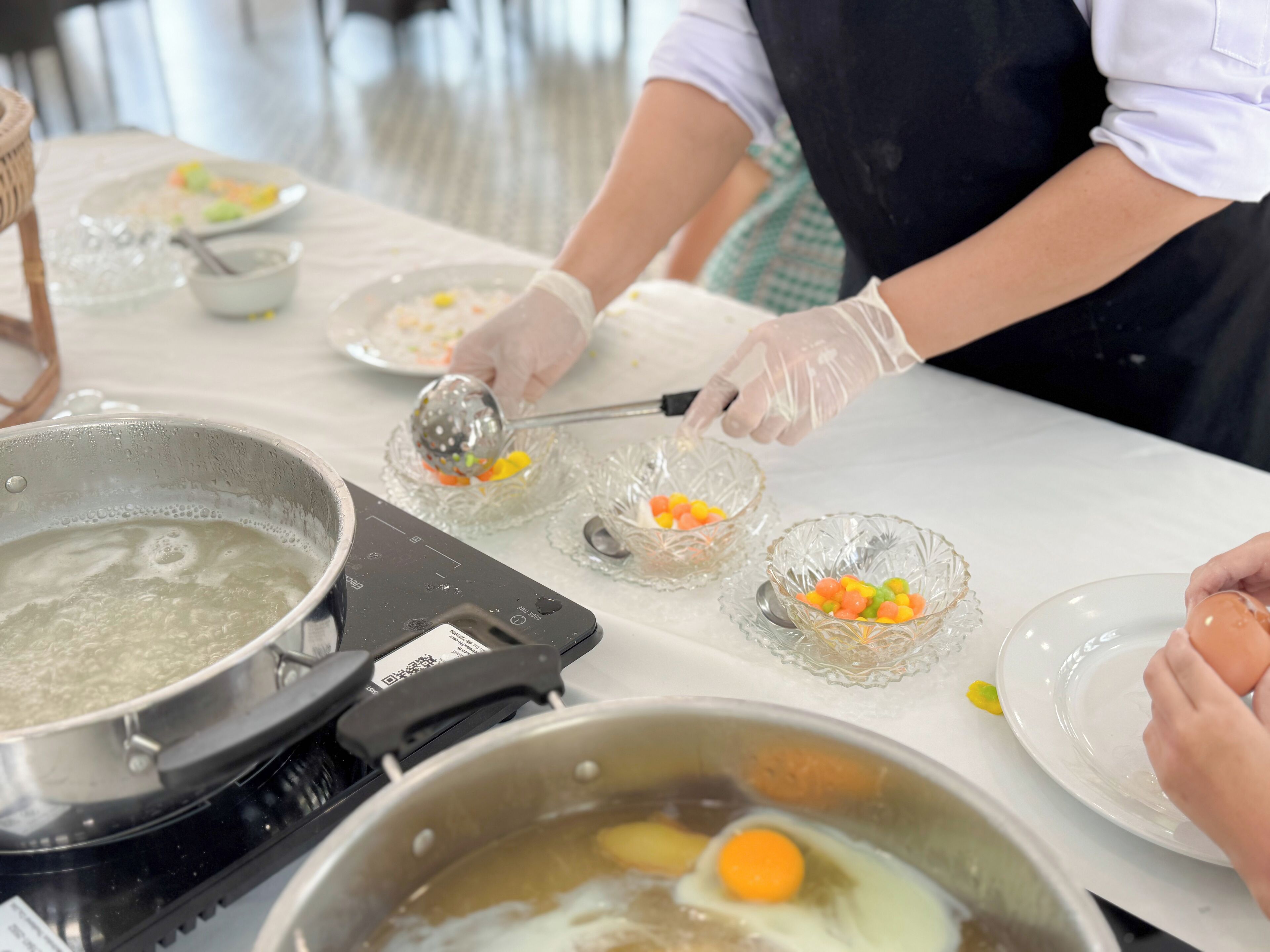 A kitchen area with a pot on a stove, bowls with colorful candies, and a person wearing gloves.